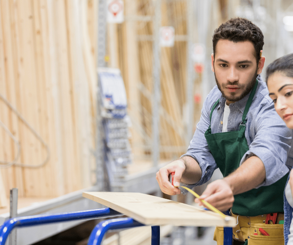 a hardware store employee helping a customer measure a piece of wood