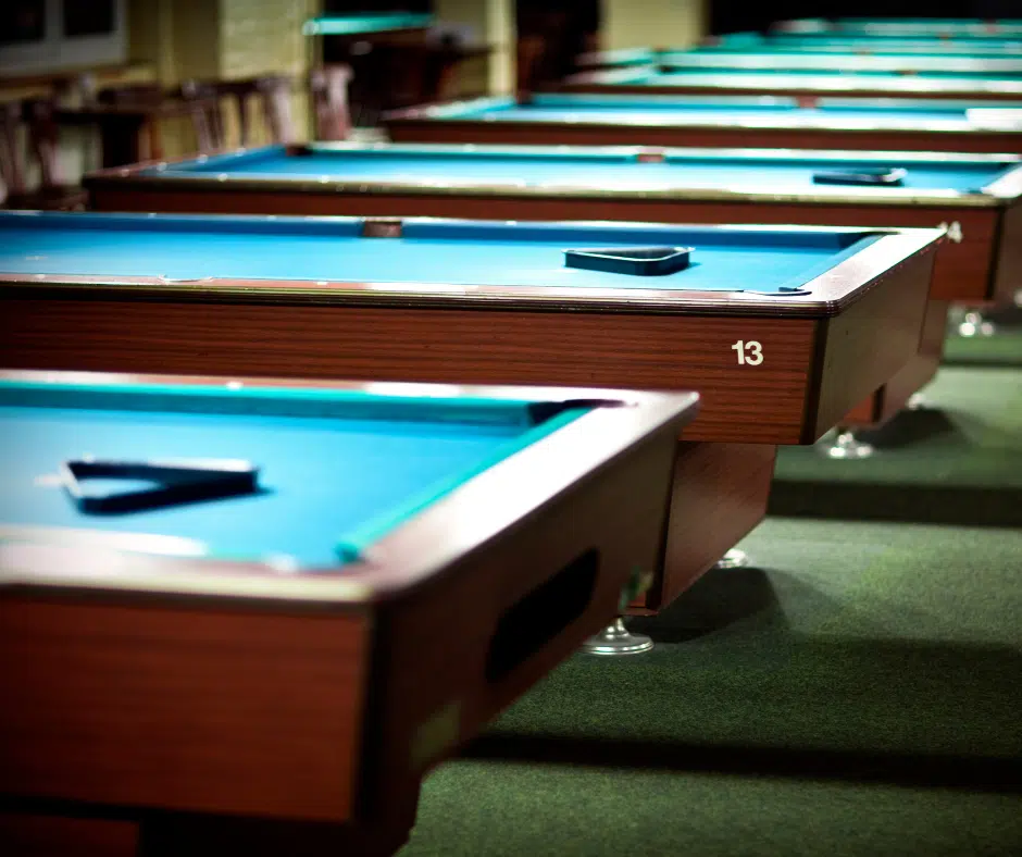 a side angle view of several pool tables in a row inside of a poll hall