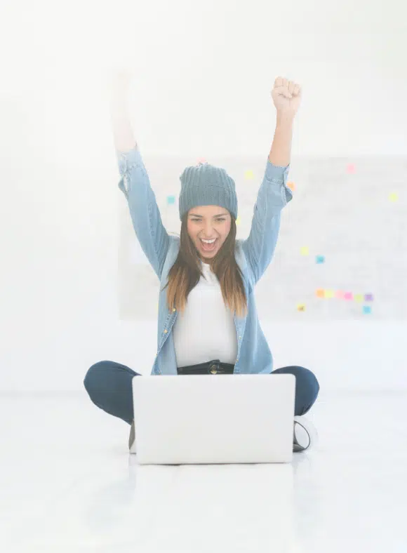 a girl sitting in front of a laptop showing excitement with her hands in the air