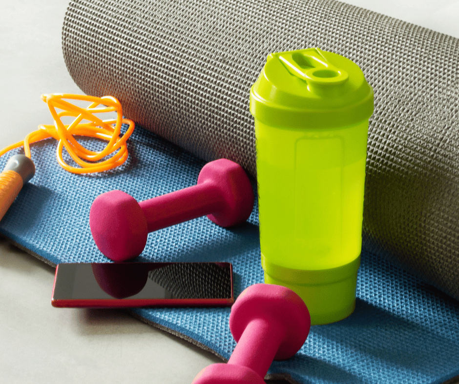 a rolled yoga mat with dumbbells, a shaker bottle, and a jump rope on it